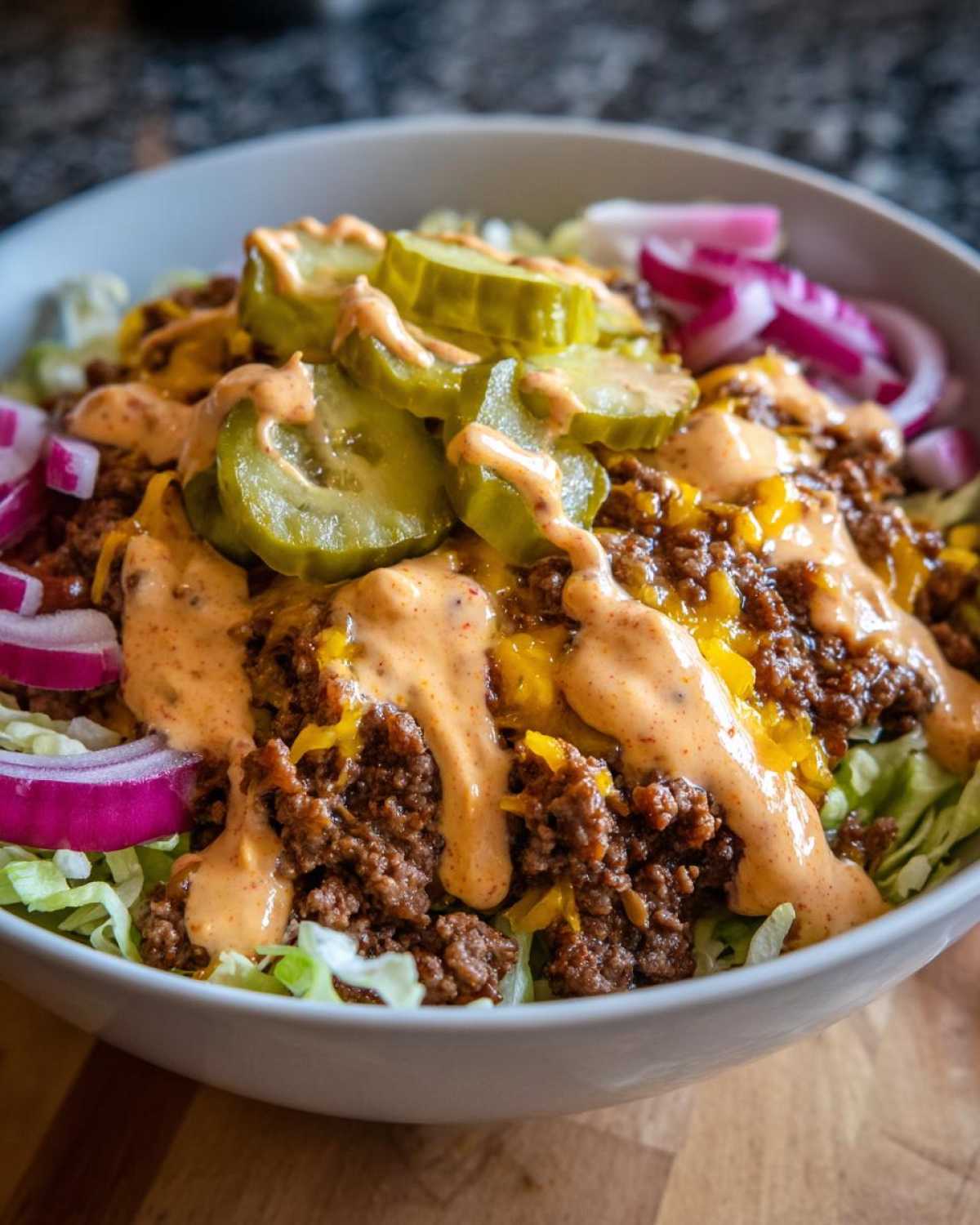 Close-up of a delicious cheeseburger bowl featuring seasoned ground beef, melted cheese, pickles, and special sauce over lettuce.