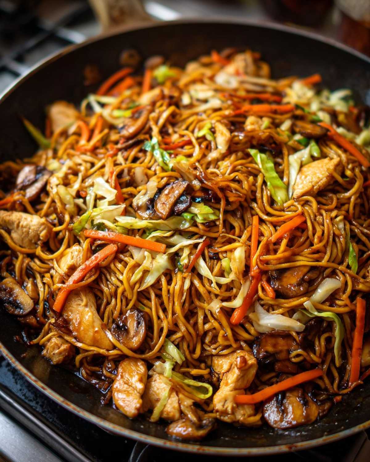 Close-up of a skillet filled with delicious chicken chow mein recipe, featuring noodles, chicken pieces, mushrooms, and shredded cabbage.