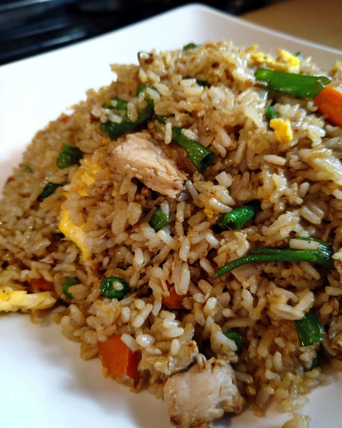 Close-up shot of a serving of amazing chicken fried rice featuring rice, diced chicken, scrambled egg, and green onions.