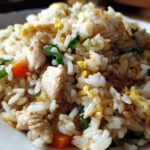Close-up macro shot of fluffy white rice mixed with chunks of chicken, scrambled egg, carrots, and green onions in chicken fried rice.