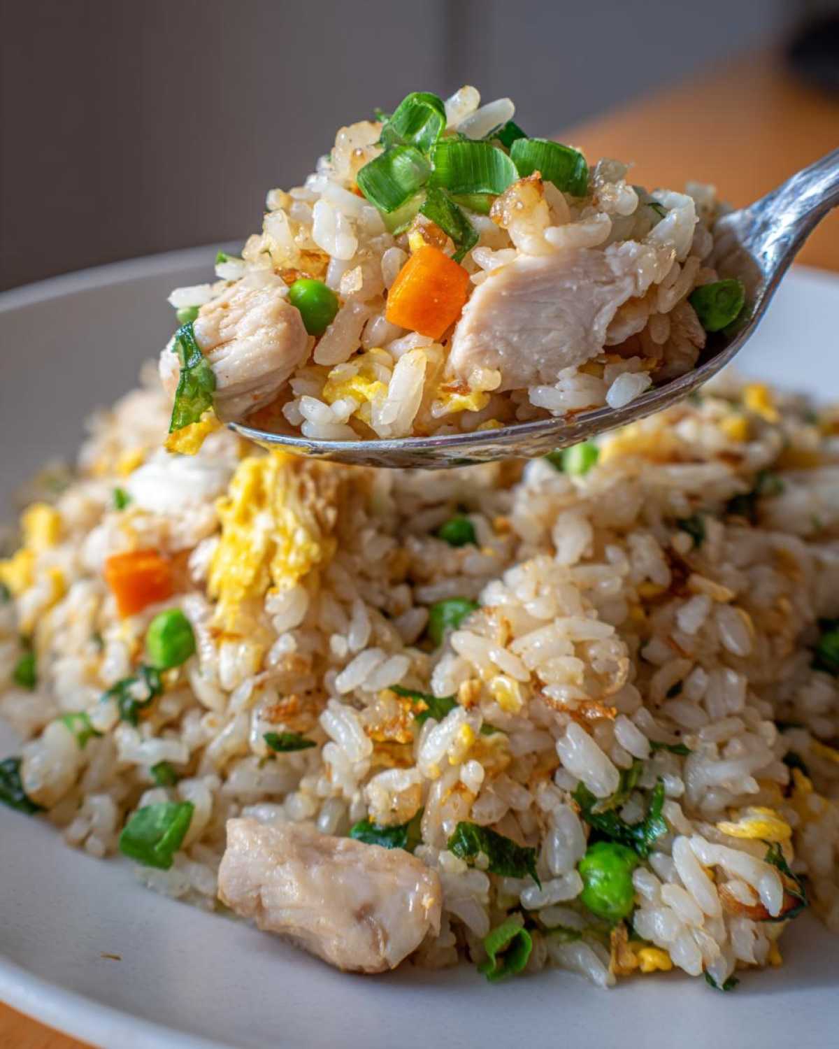 A spoonful of amazing chicken fried rice, featuring white rice, chicken pieces, carrots, peas, and green onions.