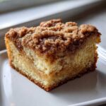 Close-up of a moist slice of coffee cake featuring a thick, buttery cinnamon crumb topping.