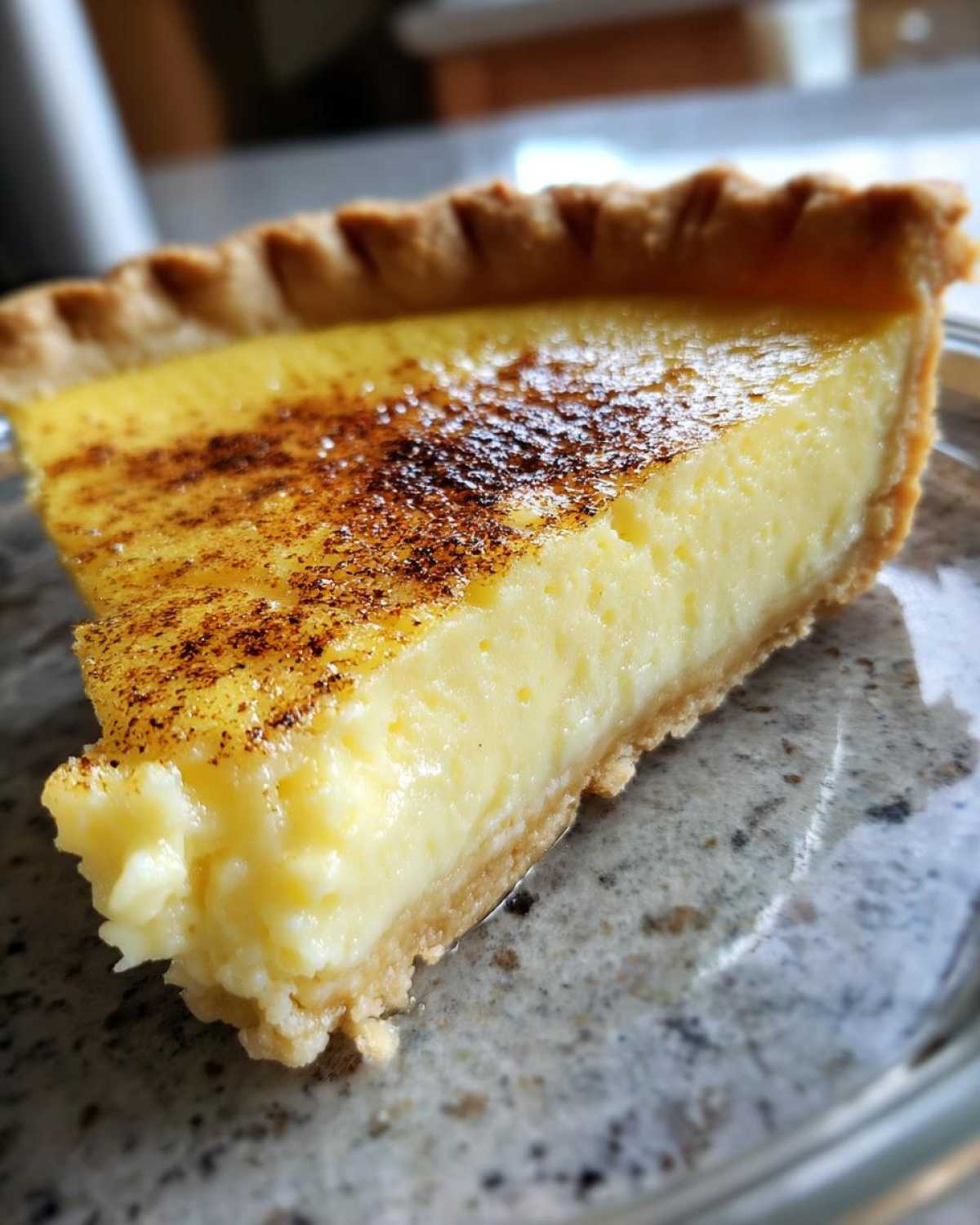 Close-up of a thick slice of creamy egg custard pie with a browned, spiced top.