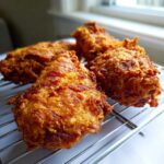 Close-up of several pieces of golden brown, crispy fried chicken resting on a wire cooling rack.