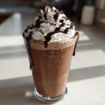 A tall glass filled with thick, blended frozen hot chocolate, topped with whipped cream and chocolate drizzle.