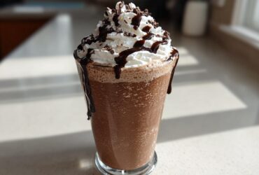 A tall glass filled with thick, blended frozen hot chocolate, topped with whipped cream and chocolate drizzle.
