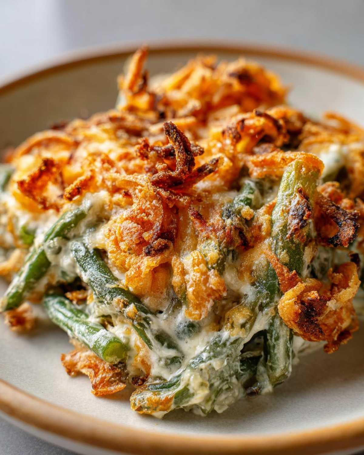 A close-up serving of creamy green bean casserole topped with golden, crispy fried onions.