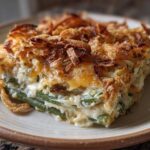 A close-up slice of amazing green bean casserole featuring creamy sauce, green beans, and a crispy fried onion topping.