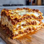 A tall, thick slice of homemade lasagna showing multiple layers of pasta, rich meat sauce, and melted cheese.