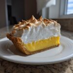 A perfect slice of lemon meringue pie showing thick, toasted meringue over bright yellow filling.