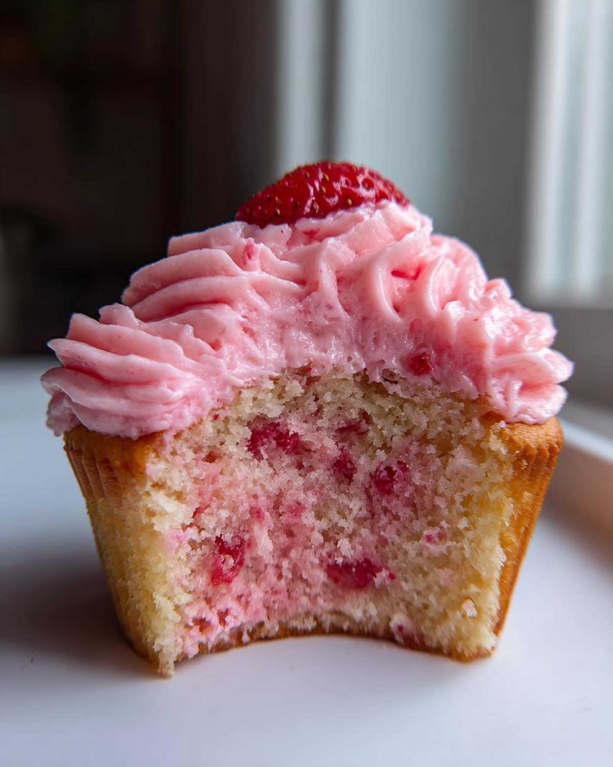 Close-up of a strawberry cupcakes cross-section showing pink frosting and strawberry pieces inside the cake.