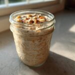 A glass jar filled with creamy apple cinnamon overnight oats, topped with nuts and spices.