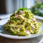 A mound of creamy avocado chicken salad mixed with chunks of red onion, topped with chives.