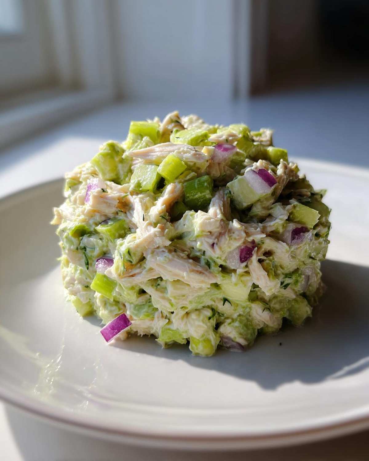 A perfectly scooped portion of creamy avocado chicken salad featuring chunks of celery and bright purple red onion.