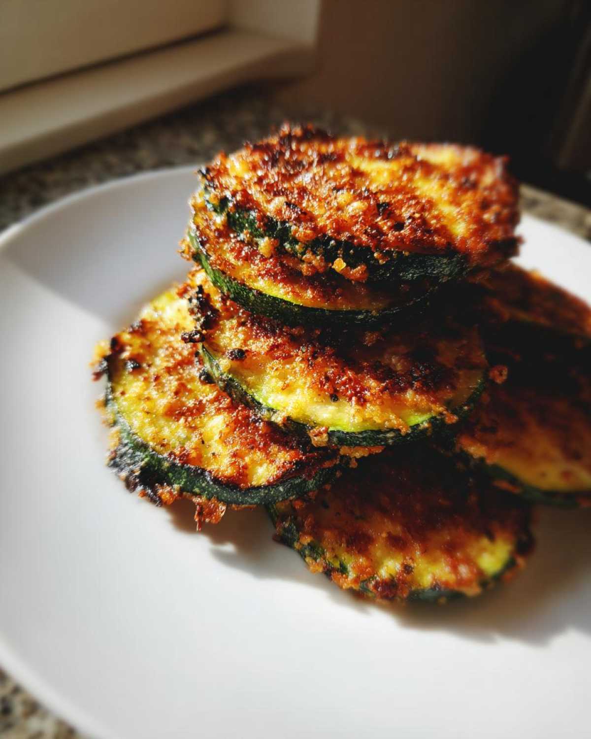 Close-up of stacked, golden-brown baked parmesan zucchini slices on a white plate.