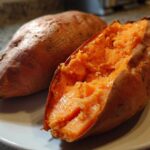 Close-up of a perfectly baked sweet potato, one split open revealing the fluffy orange interior.