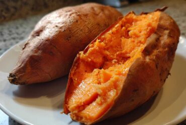 Close-up of a perfectly baked sweet potato, one split open revealing the fluffy orange interior.