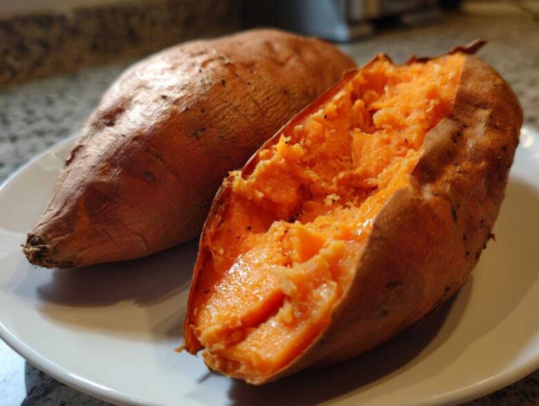 Close-up of a perfectly baked sweet potato, one split open revealing the fluffy orange interior.