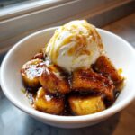 Close-up of caramelized bananas foster topped with a scoop of melting vanilla ice cream in a white bowl.