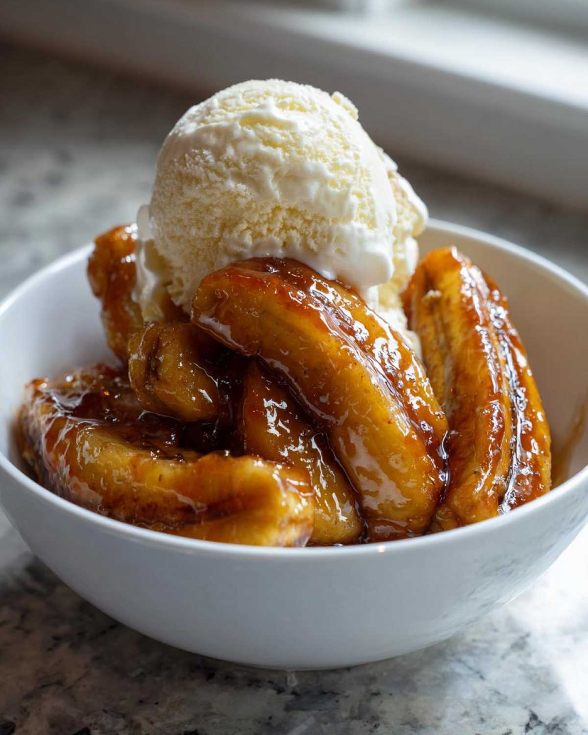 A white bowl filled with caramelized bananas in sauce, topped with a large scoop of vanilla ice cream, representing delicious bananas foster.