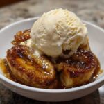 Close-up of warm Bananas Foster caramelized bananas topped with a scoop of vanilla ice cream.
