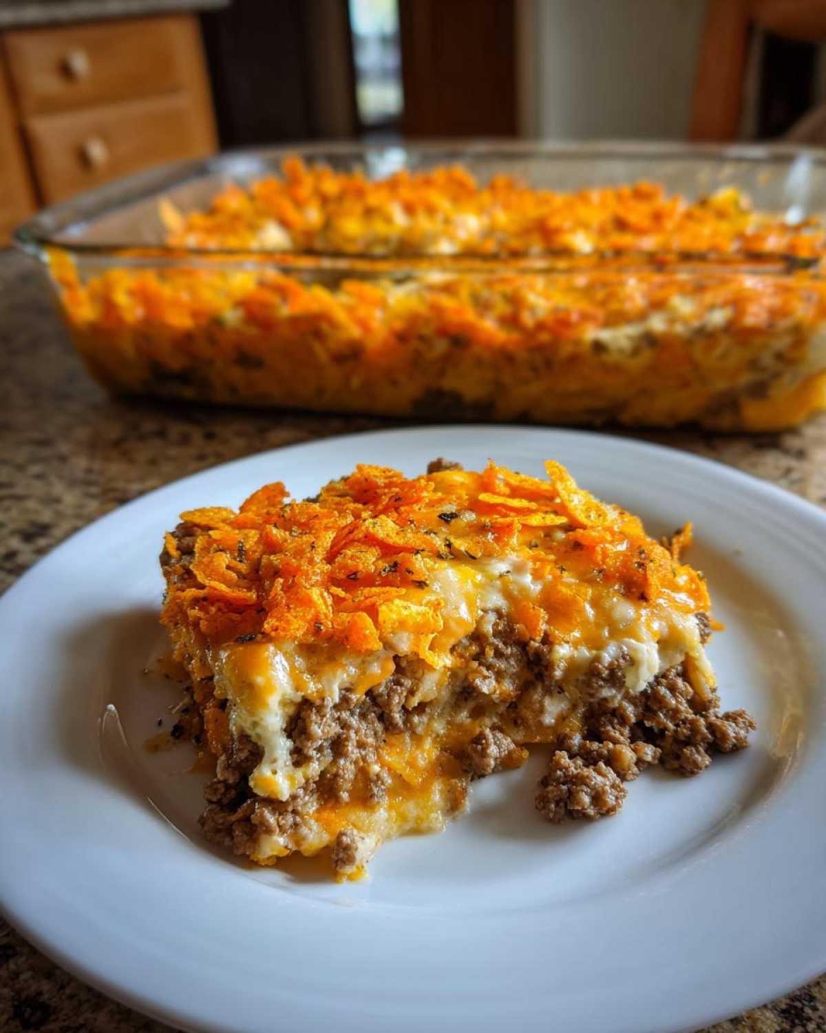 A close-up of a serving of Dorito Casserole on a white plate, showing layers of ground meat and melted cheese topped with crushed chips.