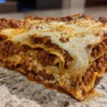 Close-up of a thick, layered slice of homemade lasagna showing rich meat sauce and melted cheese.