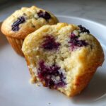 Close-up of a delicious blueberry protein muffin, one half bitten to show the moist interior and purple berry pockets.