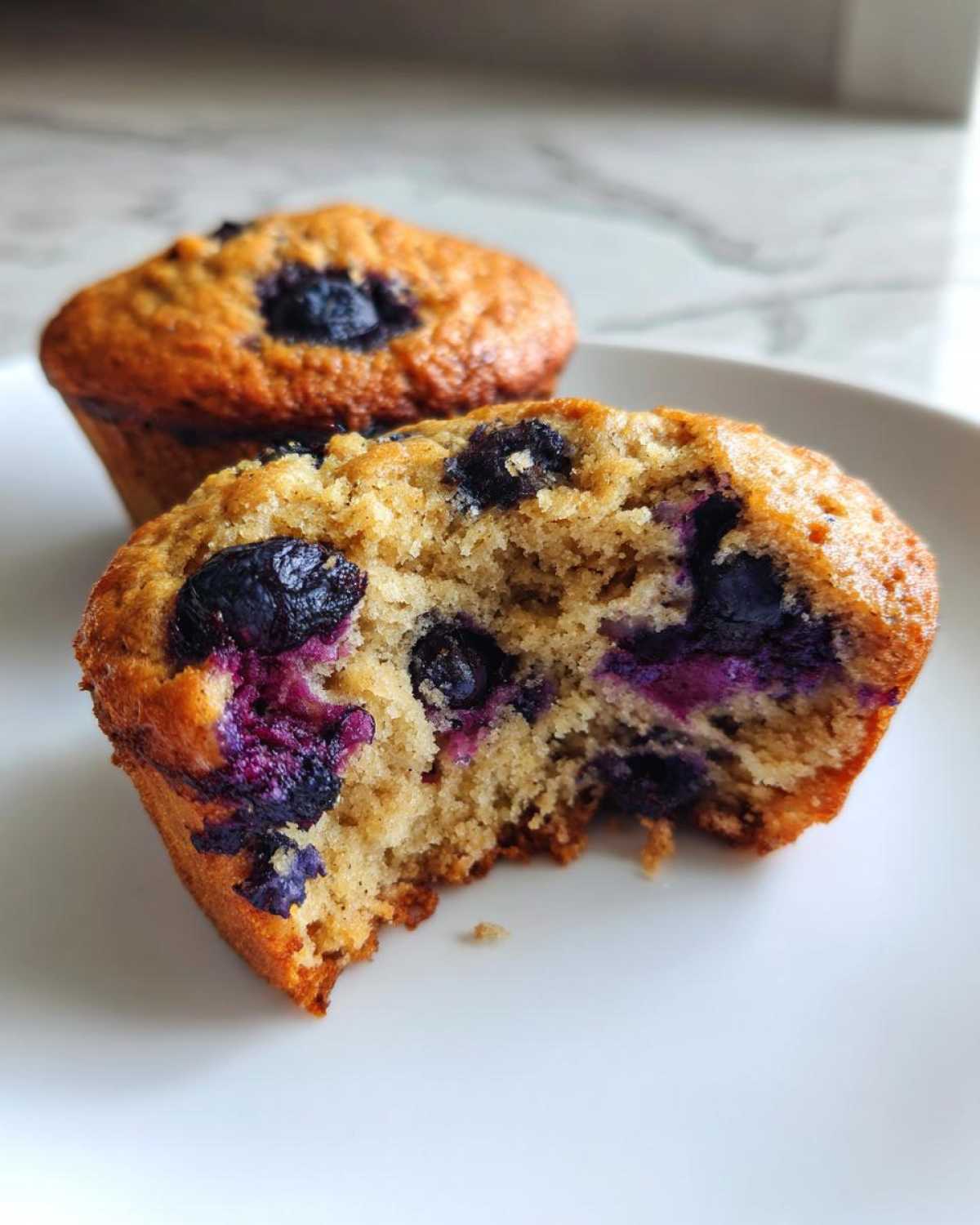 Close-up of a blueberry protein muffin cut in half showing moist texture and bursting blueberries.
