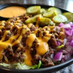 A close-up of a delicious cheeseburger bowl featuring seasoned ground beef, melted cheese sauce, diced red onion, and pickles.
