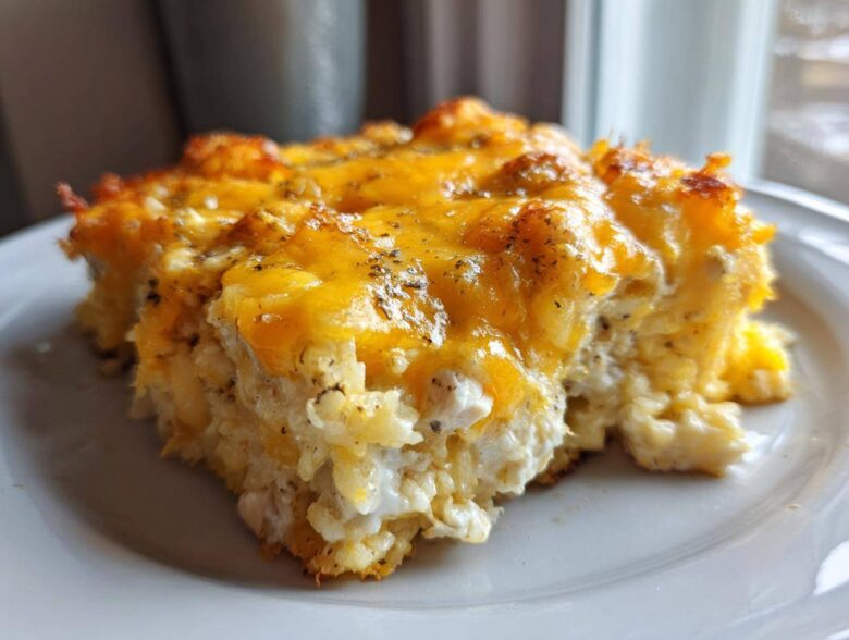 A close-up shot of a serving of cheesy chicken and rice casserole topped with melted cheddar cheese.