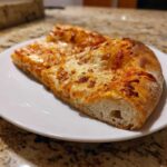 Close-up of two slices of cheesy pizza showing the airy crust made from sourdough discard pizza dough.