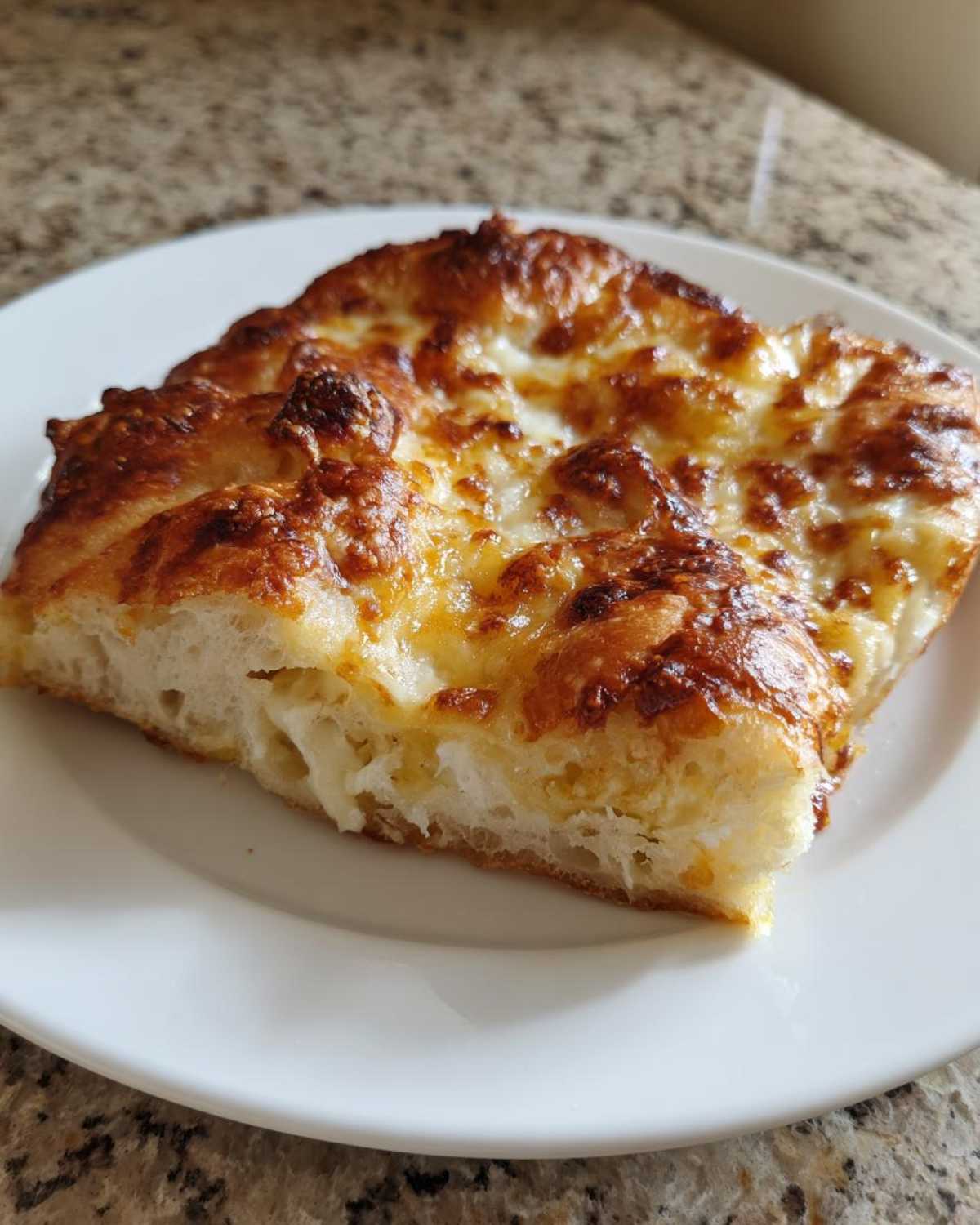 Close-up of a thick slice of cheesy pizza made with sourdough discard pizza dough, showing a golden-brown crust.