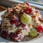 A mound of creamy chicken salad chick grape salad topped with red and green grapes and chopped pecans.