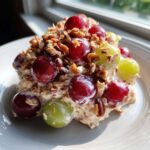 A serving of creamy grape salad, similar to chicken salad chick grape salad, topped with red and green grapes and chopped pecans.