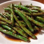 Close-up of vibrant, glossy chinese green beans with garlic sauce served in a white bowl.