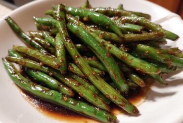 Close-up of vibrant, glossy chinese green beans with garlic sauce served in a white bowl.