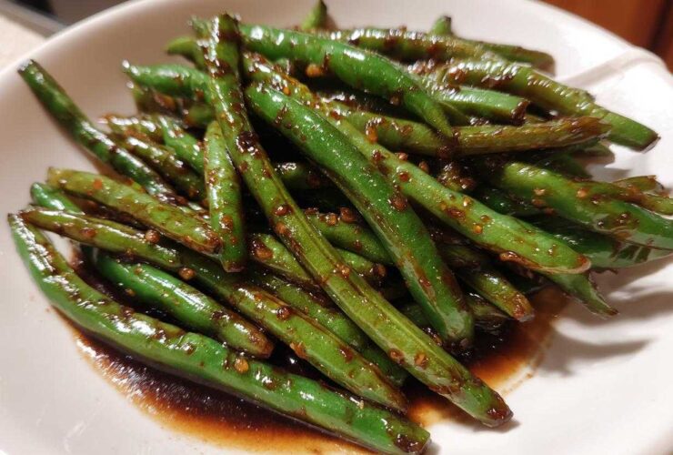 Close-up of vibrant, glossy chinese green beans with garlic sauce served in a white bowl.