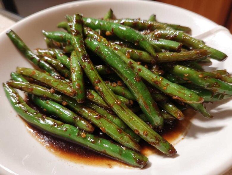 Close-up of vibrant, glossy chinese green beans with garlic sauce served in a white bowl.