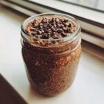 A glass jar filled with thick, dark chocolate overnight oats speckled with chia seeds, topped generously with chocolate chips.