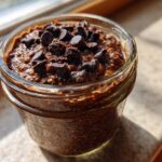 A close-up of rich chocolate overnight oats topped with dark chocolate chips in a glass jar.