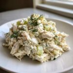 A mound of creamy cottage cheese chicken salad mixed with celery and topped with fresh dill on a white plate.