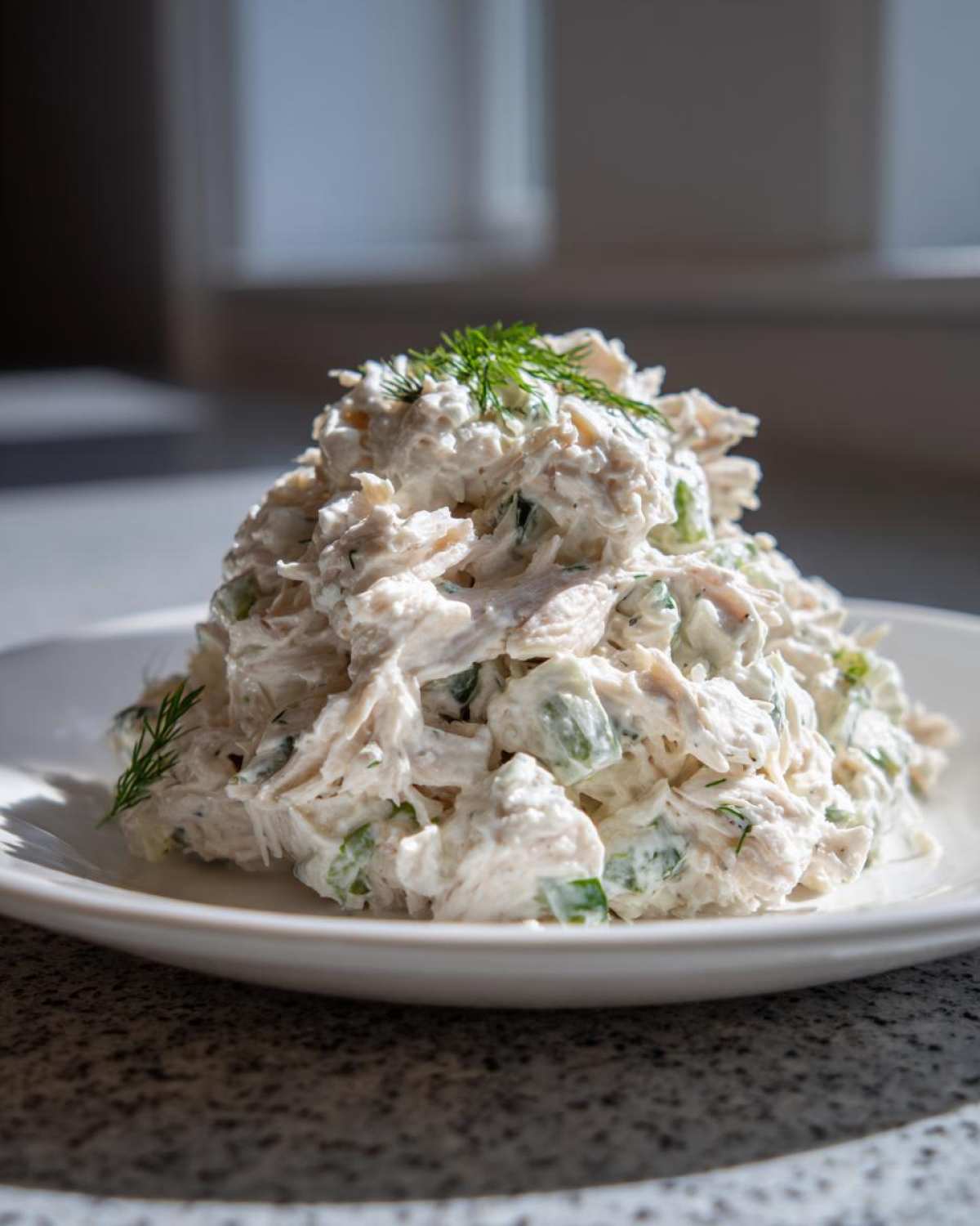 A mound of creamy cottage cheese chicken salad mixed with celery and topped with fresh dill, served on a white plate.