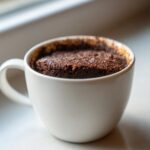 Close-up of a rich, dark Cottage Cheese Microwave Brownie baked inside a white ceramic mug.