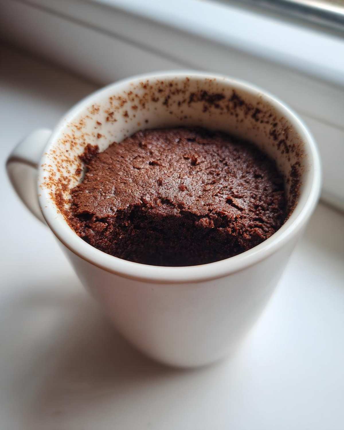 Close-up of a rich, dark chocolate Cottage Cheese Microwave Brownie baked inside a white mug.