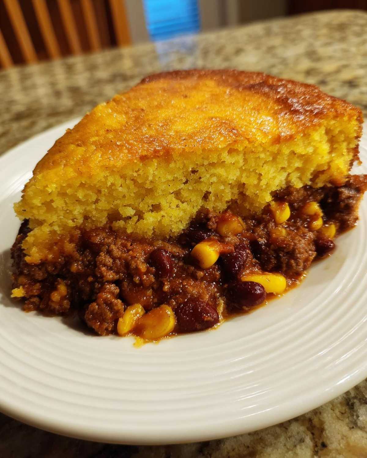 A close-up of a serving of cowboy cornbread casserole, showing the thick, golden cornbread top over a hearty chili filling with beans and corn.