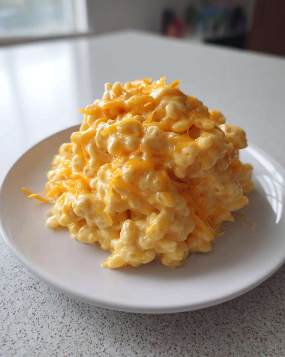 A close-up of a generous serving of creamy cheesy rice, topped with melted and shredded cheddar cheese, on a white plate.
