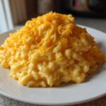 A generous serving of creamy, yellow cheesy rice topped with shredded cheddar cheese on a white plate.