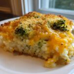 A close-up slice of creamy chicken broccoli rice casserole topped with melted cheddar cheese and breadcrumbs.
