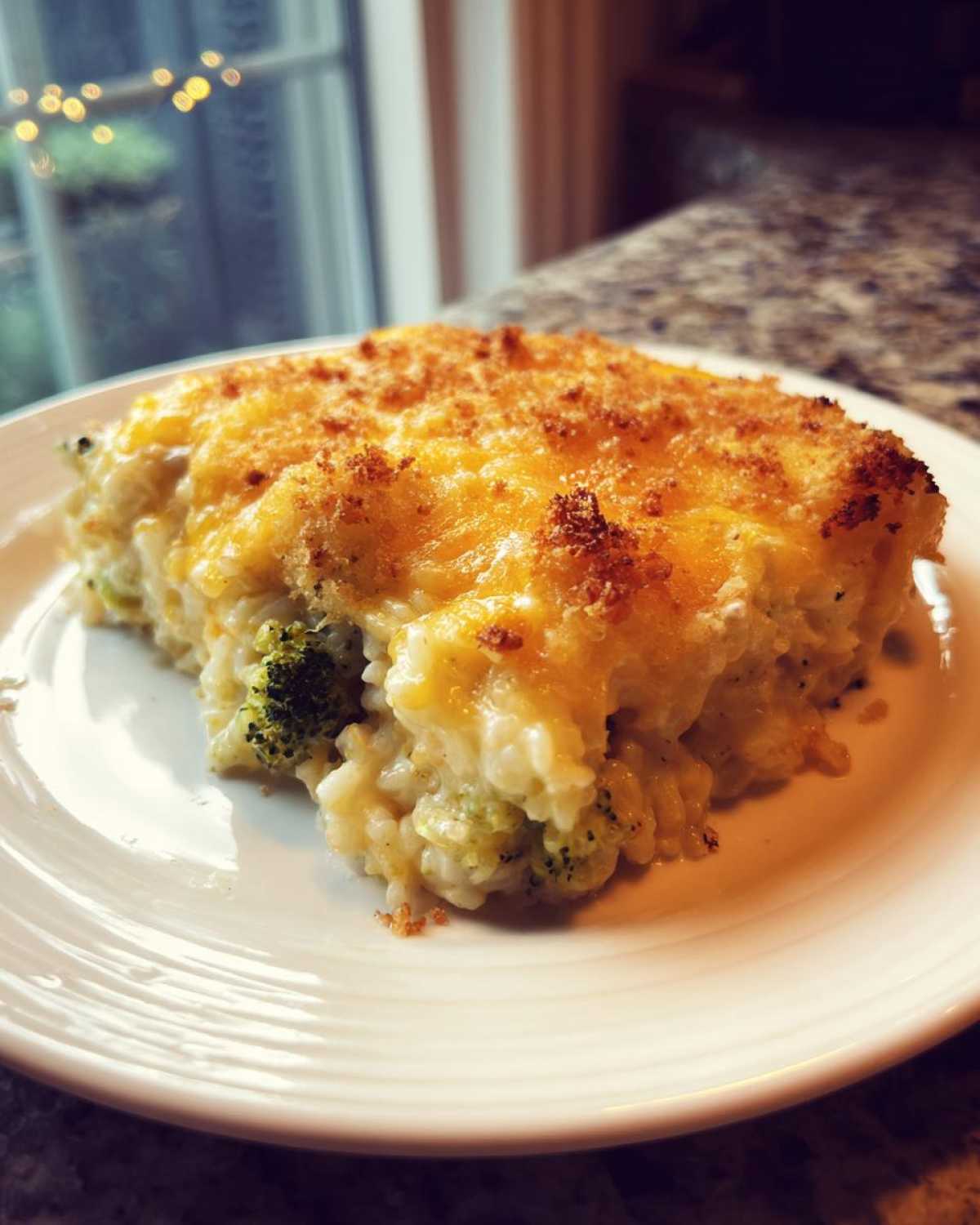 A close-up serving of creamy chicken broccoli rice casserole topped with melted, browned cheddar cheese.